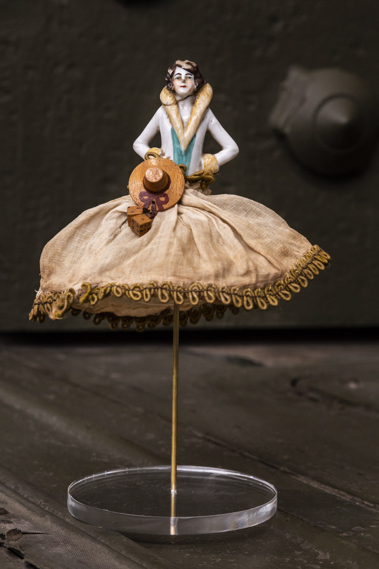 Audrey Doll_019 A vintage doll with white top and discoloured white dress. It is raised up by a long metal rod connected to a clear, circular base plate.