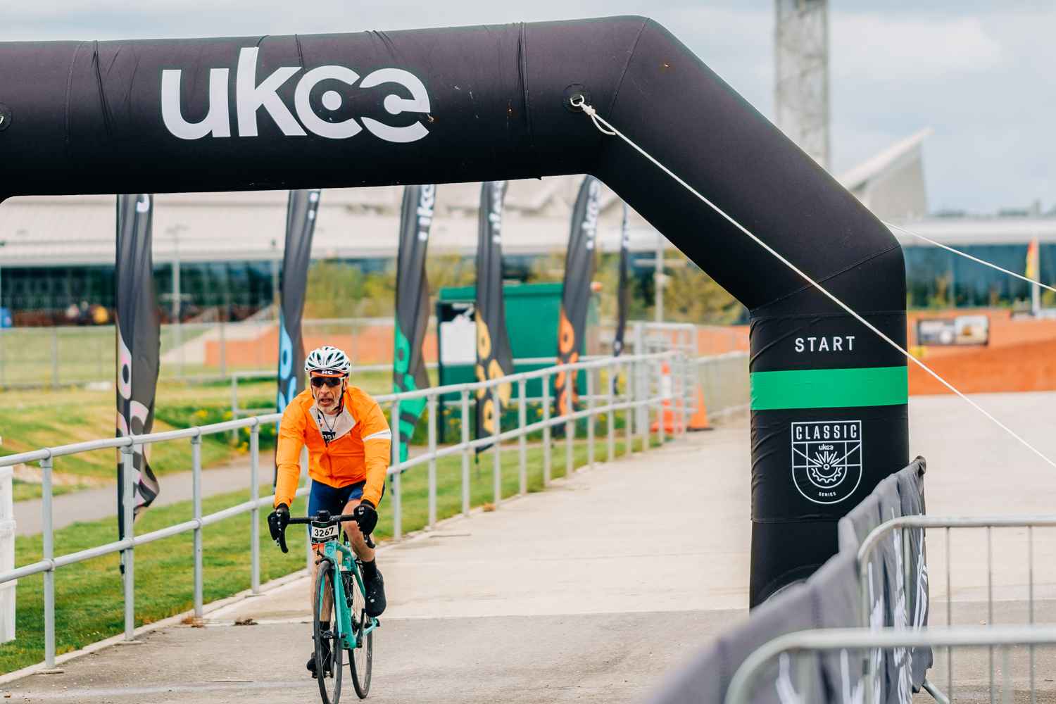 Outdoor venue hire 1500x1000 A cyclist dressed in a bright orange shirt, white helmet and blue shorts rides under an inflated, black, start sign.