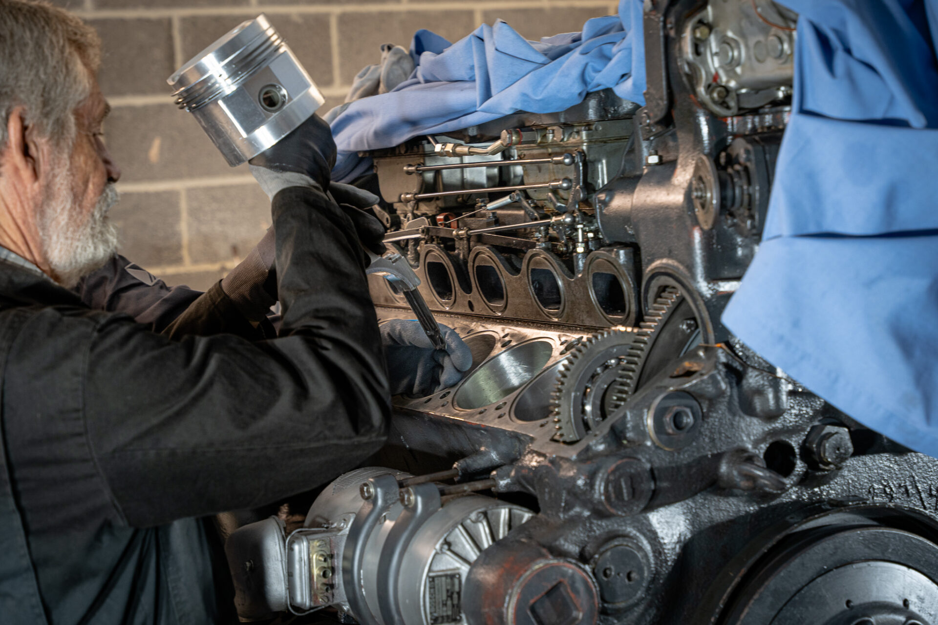 Workshop Volunteer Les Wilkins re-installing a piston and connecting rod into the engine Man holding a metal cylinder above a large engine.