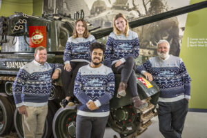 2024 Christmas Jumper Five people wearing blue Christmas jumpers posed on a tank.