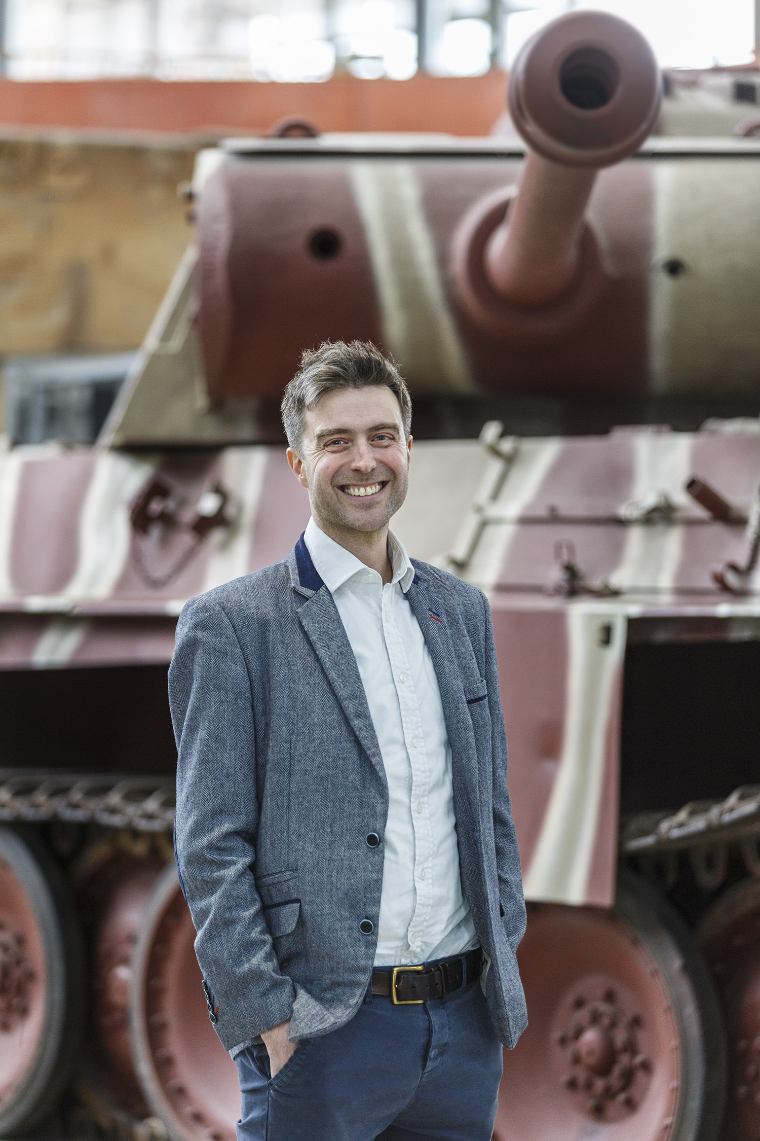 Nick Booth_001 Smiling man in a suit stood in front of a tank.