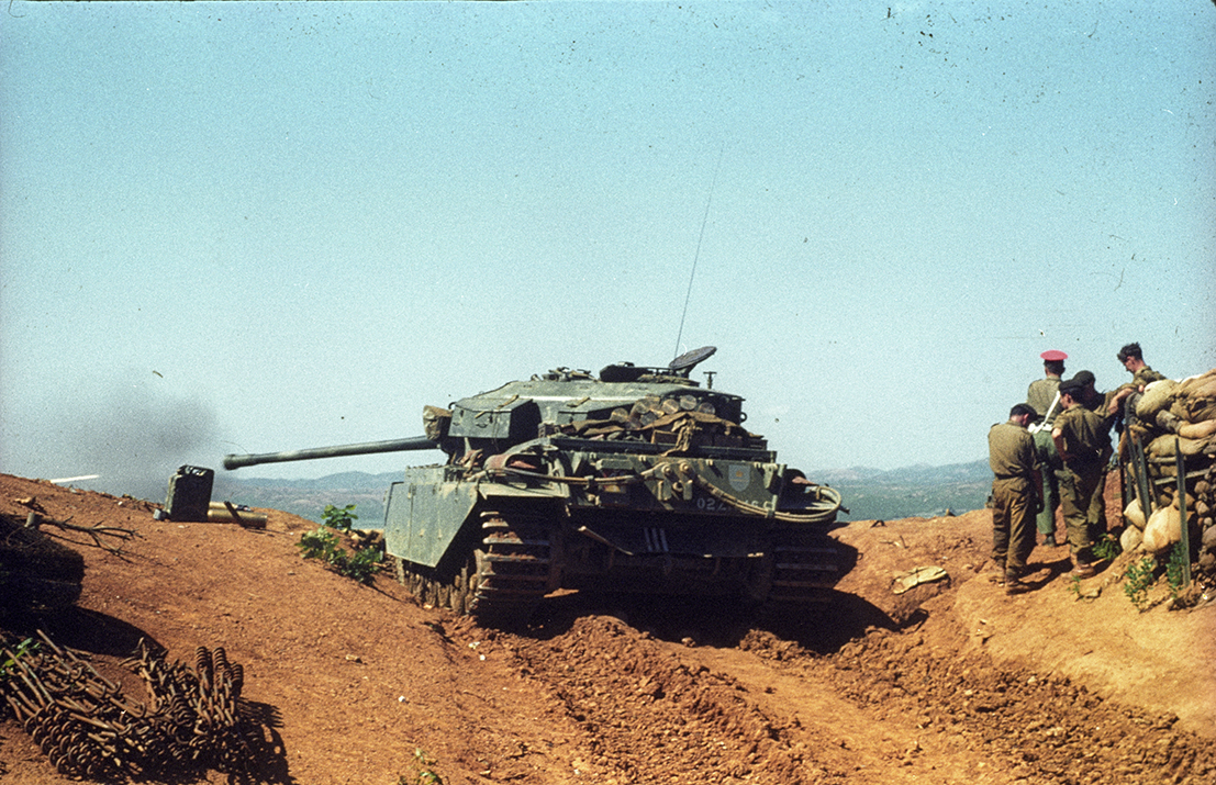 RTR in Korea Photograph of a green tank in a desert environment firing to the left.. Men in uniform stand to the right.