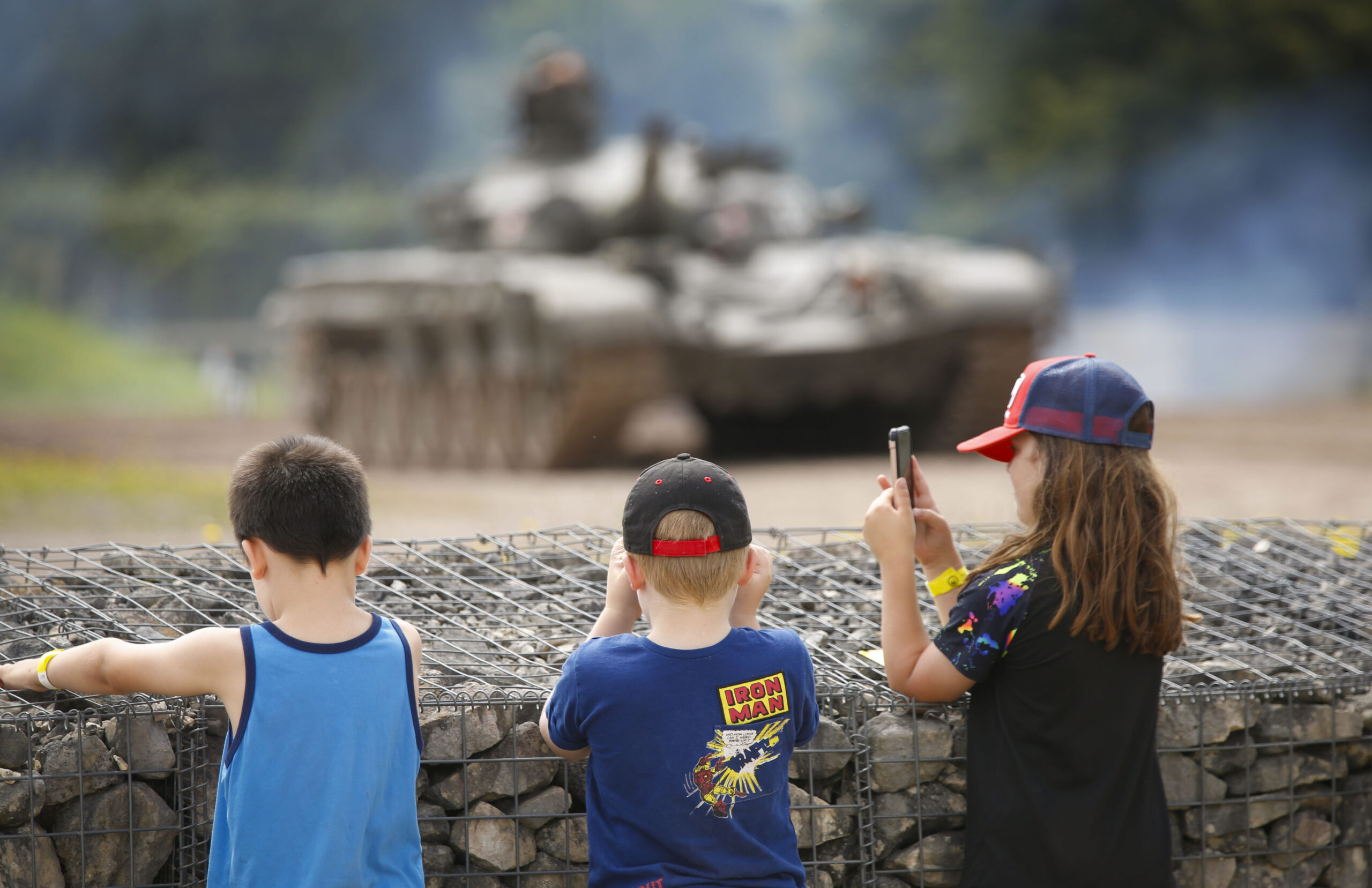 Tanks in Action 2 Three children looking over a wall at a tank.