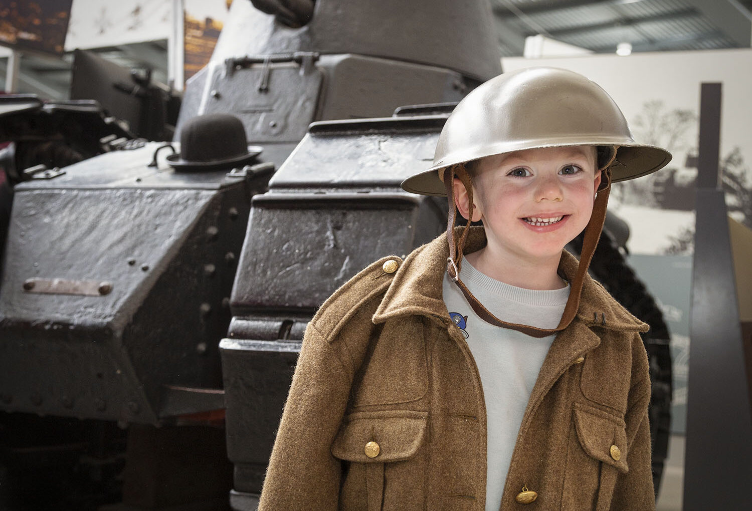 Visitors Smiling boy dressed in uniform, stood in front of a tank.