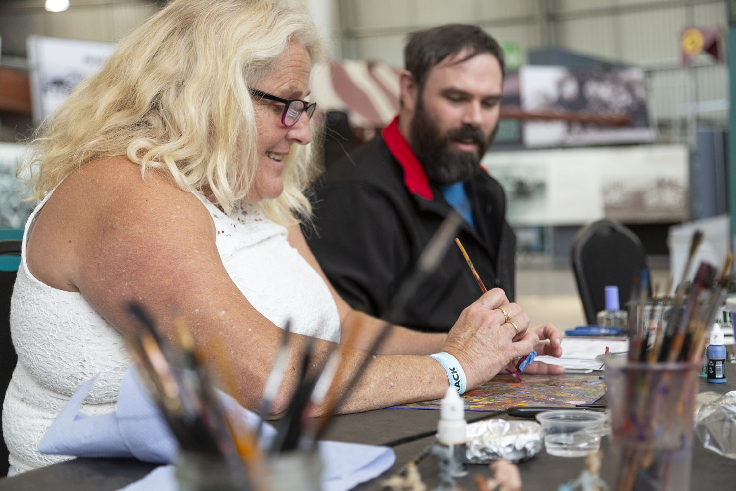On Track_062 Man and woman sat at a table painting, with pots of brushes in the foreground.