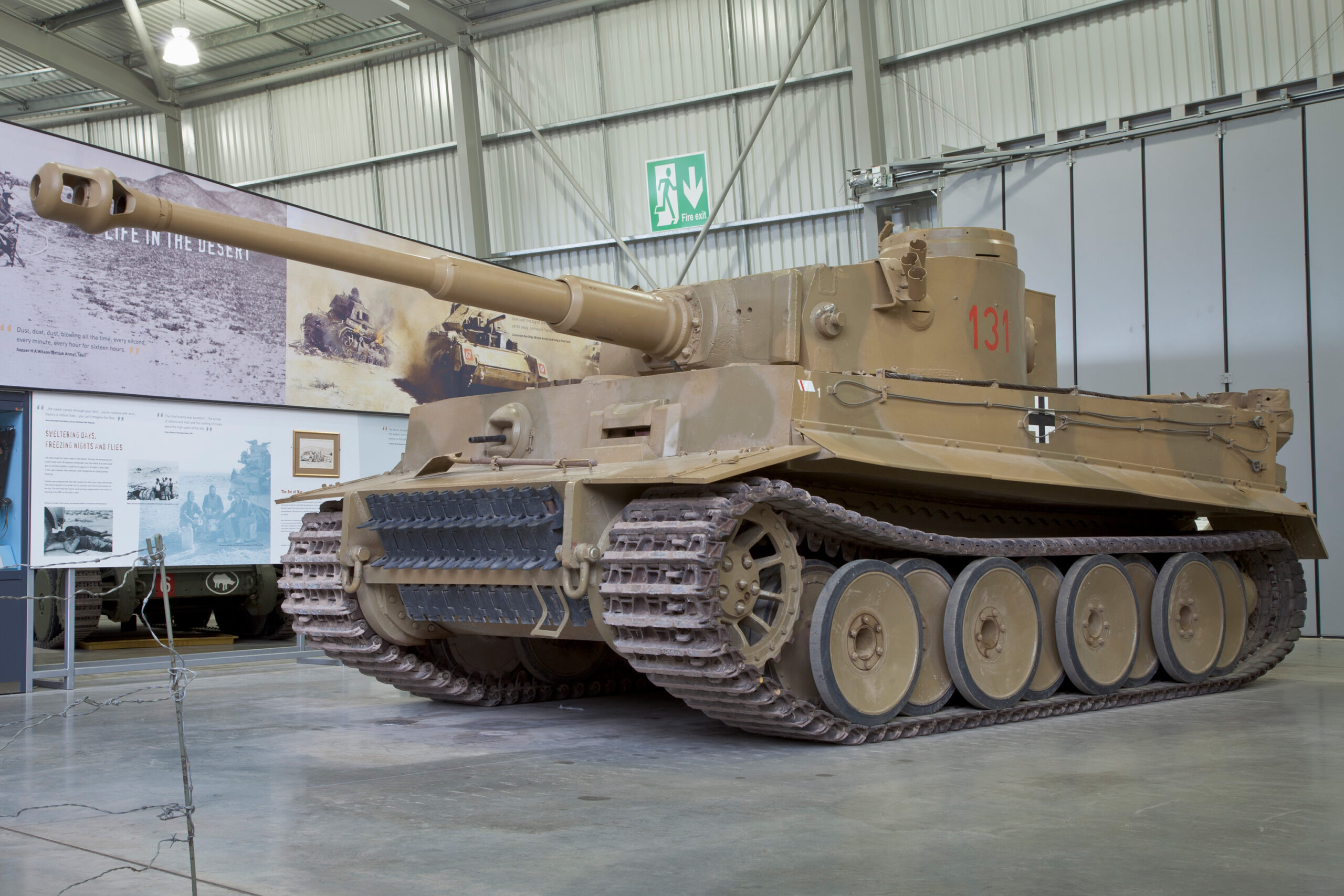 Tiger 131 on display in The Tank Museum's Tank Story Hall Dark yellow tank in exhibition space.