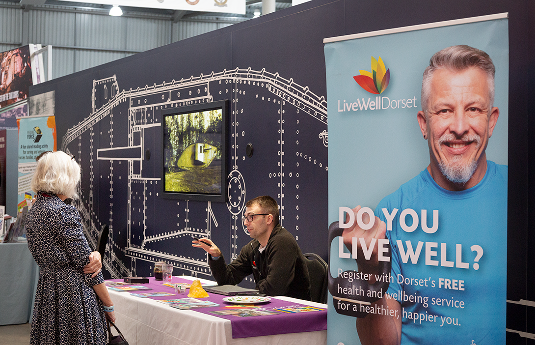 On Track 2025_005 Exhibitor table with a banner ' Do You Live Well?'.