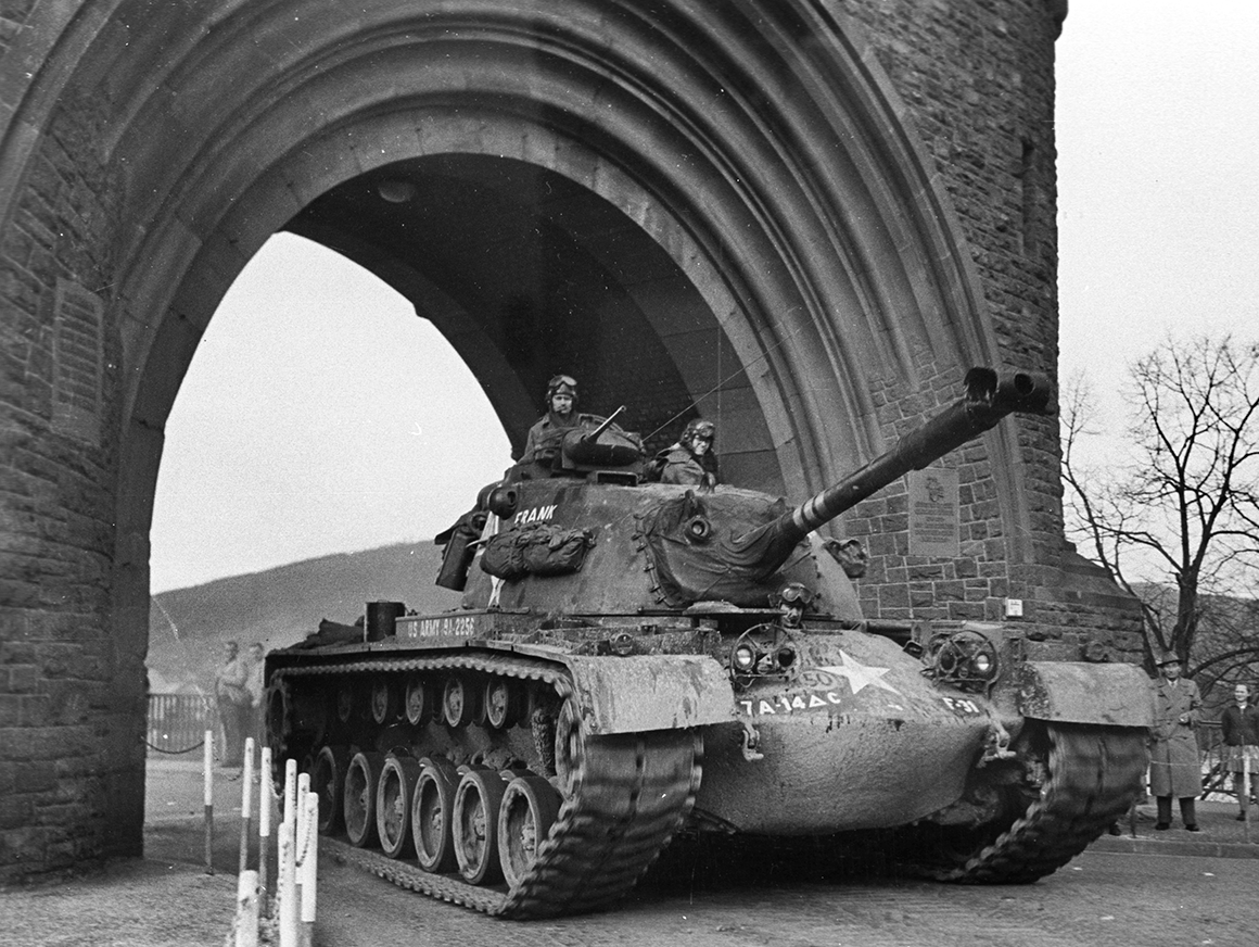 The M48A1 Black and white photo of a manned tank under a stone bridge.