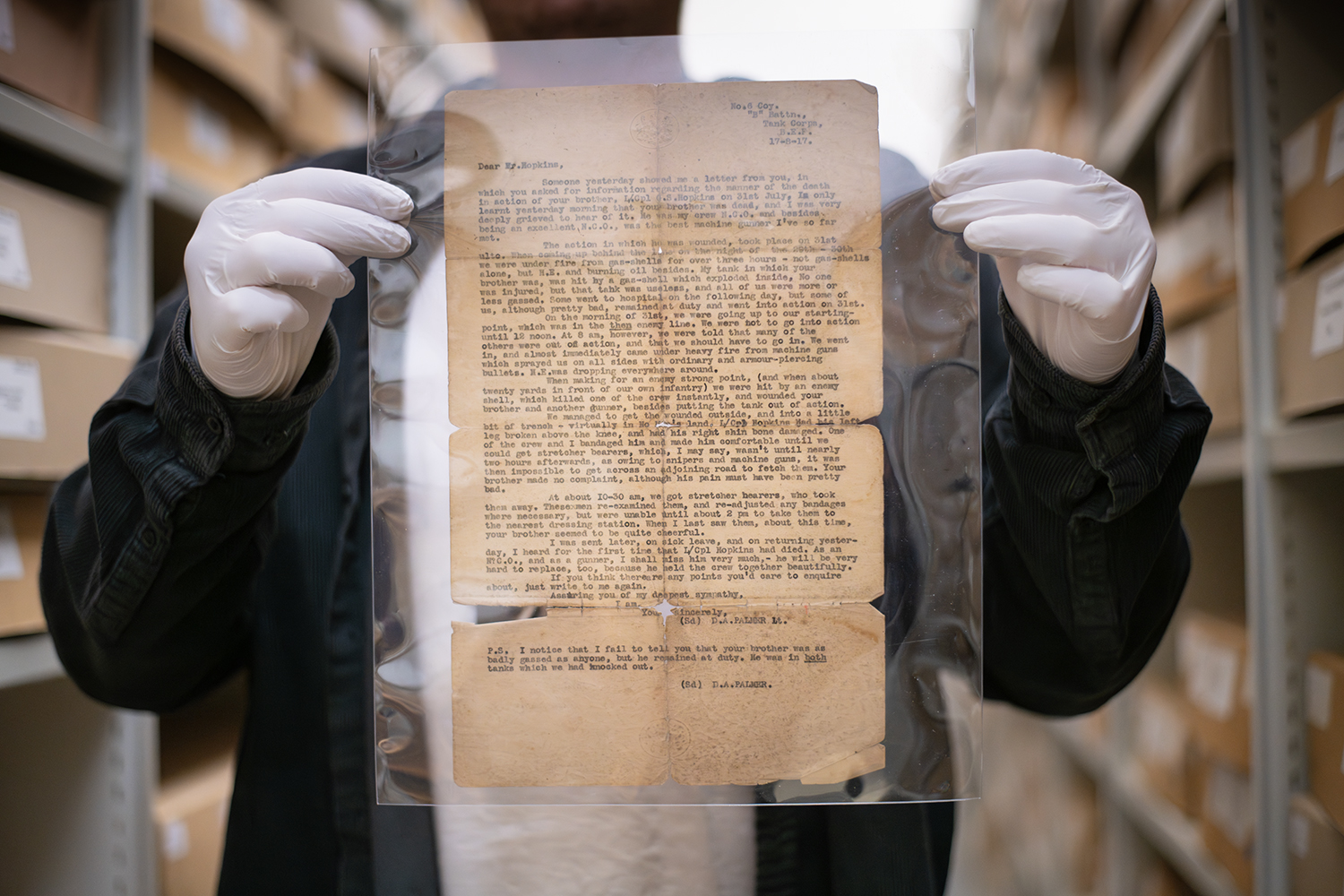 Hopkins Letter Typed letter browned and torn with age held up by a person wearing white gloves.